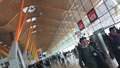 Air-crew-members-passing-by,-tilted-dolly-shot-inside-airport-terminal-area,-with-passengers-in-background,-people-walking-towards-boarding-gates-at-Madrid-Barajas-Airport