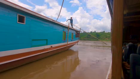 A-local-sailor-pushes-the-boat-away-from-the-shore,-launching-it-down-the-Mekong-river-with-tourists-on