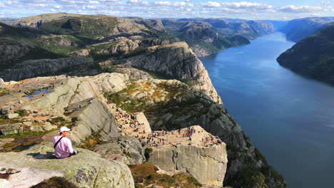 Traveller-enjoying-the-scenic-beautiful-view-of-Preikestolen-Pulpit-Rock-next-to-a-lake-body