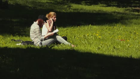 Two-young-women-sit-on-the-lawn-talking-and-enjoying-a-sunny-and-windy-summer-afternoon