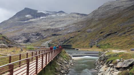 Handheld-dolly-shot-of-Istra-river-and-the-modern-walkways-at-Trollstigen-in-Norway,-water-barriers-control-the-flow-of-water,-tourists-walking-on-the-pathway,-mountains-in-background