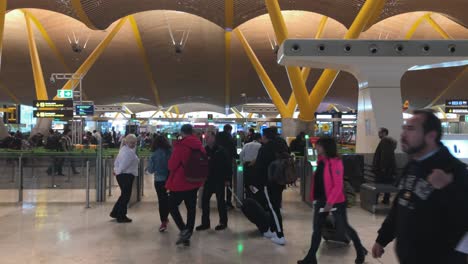 Menschen-Stürmen-Durch-Den-Terminalbereich-Des-Internationalen-Flughafens-Madrid-Barajas-Und-Passieren-Die-Sicherheitskontrolle-Zu-Ihren-Check-in-Schaltern,-Schwenk-Von-Links-Nach-Rechts