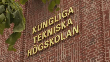 Gold-lettering-on-a-red-brick-wall-with-green-leaves-blowing-gently-in-the-foreground