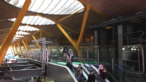 Modernes-Flughafenterminal-Mit-Menschen,-Die-Rolltreppen-Benutzen,-Zeitgenössisches-Architektonisches-Design,-Das-Stahl-Und-Holz-Mit-Großen-Durchscheinenden-Fenstern-In-Der-Decke-Kombiniert,-Reisen,-Transport-Und-Architektur