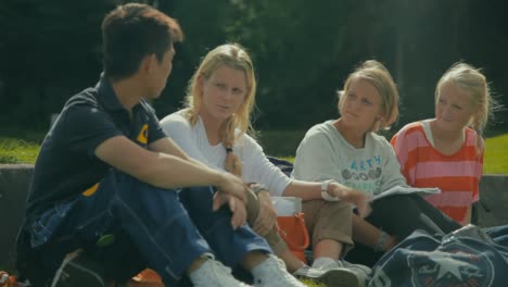 Three-blonde-women-sitting-outside-in-the-sunshine-and-chatting-with-a-young-Asian-man