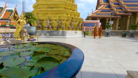 Slow-motion,-tracking-shot-of-a-pot-full-of-lupines,-in-front-monks-walking-at-the-grand-palace-of-Bangkok,-on-a-sunny-day,-in-Thailand,-Asia