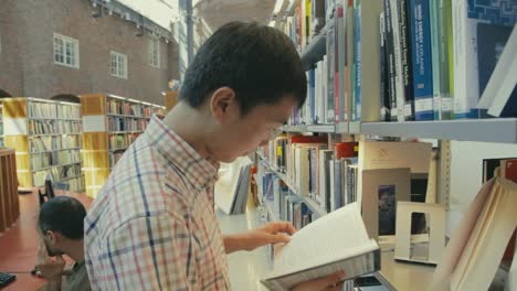 Ein-Junger-Asiatischer-Mann-Betrachtet-Ein-Buch-Im-Regal-Der-Universitätsbibliothek