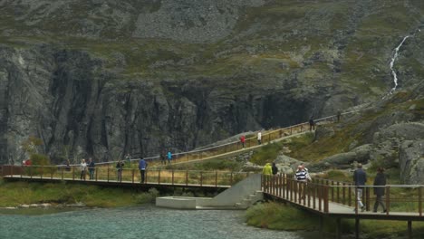 Tourists-walking-on-modern-walkways-on-top-of-Troll's-ladder-in-Norway-next-to-a-mountain-stream,-the-pathways-offer-easy-access-to-tourists-to-the-tip-of-the-cliffs-with-viewpoints-on-the-waterfalls