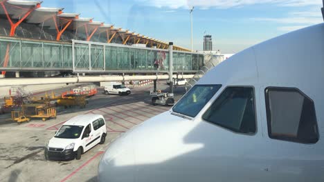 Nase-Eines-Modernen-Verkehrsflugzeugs,-Eine-Passagierbrücke-Im-Hintergrund,-Menschen,-Die-Ein-Flugzeug-Besteigen,-Servicefahrzeuge-Auf-Dem-Rollfeld,-Transport--Und-Reisekonzept,-Flughafen-Madrid-Barajas