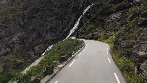 A-bus-driving-down-a-narrow-mountain-road-and-approaching-the-Stigfossen-waterfall-at-Tolls-ladder-or-Trollstigen-in-Norway,-a-popular-tourist-and-hiking-destination-in-Scandinavia
