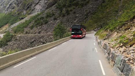 A-red-and-black-painted-tourist-bus-driving-up-a-narrow-mountain-road,-stopping-to-let-the-downward-bus-to-pass-by,-driving-experience-on-the-Trolls-ladder-road-in-Norway