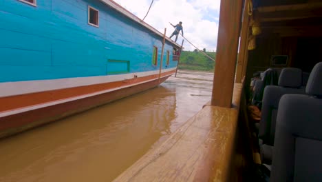 A-local-man-pushes-the-boat-away-from-the-shore,-launching-it-down-the-Mekong-river