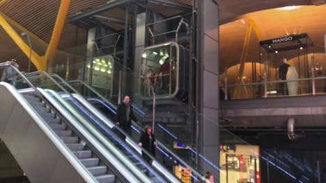 Passagiere-Mit-Handgepäck-Betreten-Die-Rolltreppe-In-Einem-Modernen-Gebäude,-Dem-Hauptterminal-Des-Internationalen-Flughafens-Madrid-Barajas-Mit-Seinem-Modernen-Architektonischen-Design-Und-Dem-Flugreisekonzept