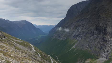 Adult-male-taking-pictures-with-his-smartphone-in-the-scenic-landscape-of-Norwegian-mountains-and-waterfalls-at-Trollstigen,-winding-mountain-road-beneath-and-towering-mountains-in-the-background