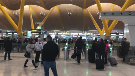 Schwenkaufnahme-Des-Innenraums-Eines-Geschäftigen-Flughafens,-Menschen,-Die-Mit-Ihrem-Gepäck-Zu-Allen-Seiten-Eilen,-Check-in-Gates-Im-Hintergrund,-Flughafen-Madrid,-Reise--Und-Transportkonzept