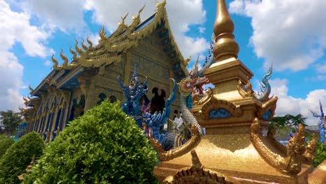 Moving-shot-tracking-the-blue-temple,-behind-bushes-and-objects,-on-a-sunny-day,-in-Chiang-Rai,-Thailand,-Asia