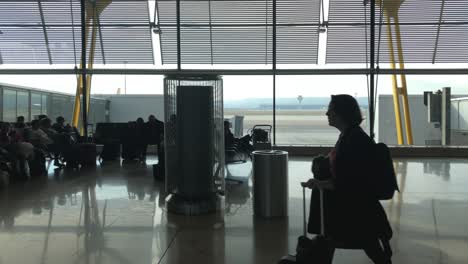 Menschen,-Die-Im-Flughafenterminal-Gehen-Und-Sitzen,-Verschiebbare-Dolly-Aufnahme-Von-Silhouetten-Von-Passagieren,-Fluggastbrücken-Und-Asphalt-Im-Hintergrund,-Reise--Und-Transportkonzept,-Flughafen-Madrid-Barajas
