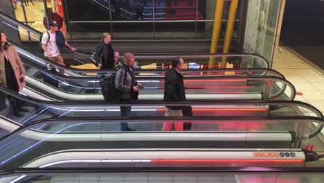 Escalator-staircase-in-busy-station-terminal-area-or-airport,-people-riding-and-walking-off,-carrying-their-luggage