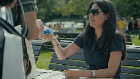 Pretty-young-woman-wearing-sunglasses-sits-on-a-bench-and-completes-a-registration-form-before-giving-it-back