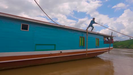 Ein-Einheimischer-Seemann-Schiebt-Ein-Boot-Vom-Ufer-Weg-Und-Lässt-Es-Mit-Touristen-An-Bord-Den-Mekong-Hinunterfahren