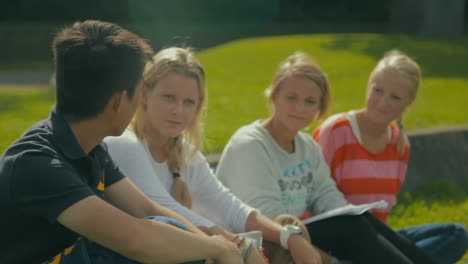 An-Asian-man-talks-with-three-blonde-women-sitting-outside-in-the-sunshine