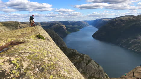 Hikers-setting-up-gear-with-a-pan-towards-a-crowd-of-tourists-downhill-at-Preikestolen-Pulpit-Rock-Norway