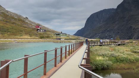 Handheld-dolly-shot-walking-towards-a-group-of-tourist-on-a-modern-walkway-in-natural-landscape-above-a-mountain-river,-Trollstigen-or-Trolls-ladder-in-Norway,-a-popular-destination-in-Scandinavia