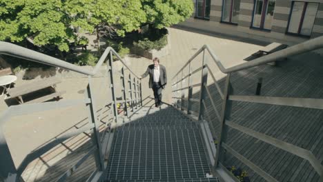 Man-dressed-in-a-suit-walks-up-metal-stairs-on-the-outside-of-a-building