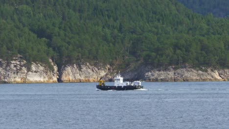 Wide-view-of-a-small-barge-carrying-a-large-excavator-making-way-across-a-Norwegian-fjord