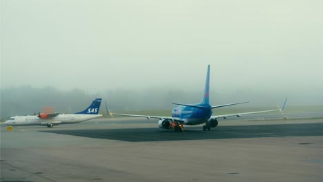 An-airplane-passing-in-front-of-a-stationary-airplane-on-the-runway-on-a-foggy-day-at-Stockholm-Arlanda