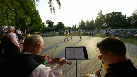 Fröhliche-Und-Lächelnde-Skandinavier-Führen-Einer-Zuschauermenge-Die-Sehr-Traditionelle-Kunst-Des-Volkstanzes-Vor,-Während-Musiker-Geige-Spielen