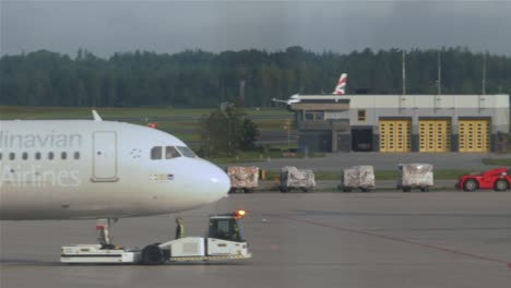 Ein-Gepäckwagen-Mit-Fünf-Vollgepackten-Waggons,-Der-über-Den-Taxistreifen-Fährt-Und-In-Stockholm-Arlanda-Hinter-Einem-Flugzeug-Auftaucht