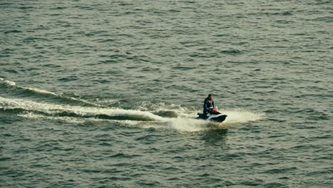 Man-wearing-a-wet-suit-while-riding-on-a-personal-watercraft-speeding-across-the-water