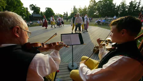 Fröhliche-Und-Lächelnde-Skandinavier-Führen-Einer-Zuschauermenge-Die-Sehr-Traditionelle-Kunst-Des-Volkstanzes-Vor,-Während-Musiker-Geige-Spielen