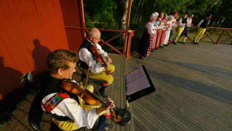 Fröhliche-Und-Lächelnde-Skandinavier-Führen-Einer-Zuschauermenge-Die-Sehr-Traditionelle-Kunst-Des-Volkstanzes-Vor,-Während-Musiker-Geige-Spielen