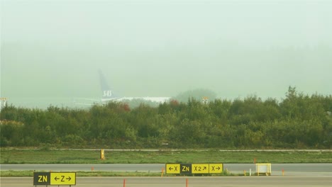 An-airplane-moving-on-the-airfield-behind-some-green-bushes-almost-covered-in-fog-at-Stockholm-Arlanda