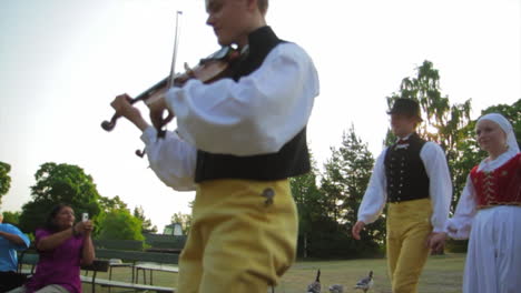 Fröhliche-Und-Lächelnde-Skandinavier-Führen-Einer-Zuschauermenge-Die-Sehr-Traditionelle-Kunst-Des-Volkstanzes-Vor,-Während-Musiker-Geige-Spielen