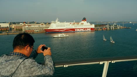 Asian-tourist-taking-photos-of-a-big-ferry-moored-on-the-helsinki-harbor-from-another-ferry