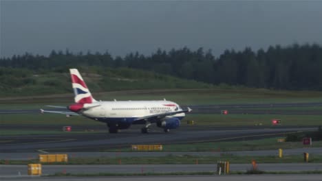 Passenger-aircraft-of-British-Airways-moving-towards-take-off-on-the-runway-of-Stockholm-airport-in-Sweden,-with-ground-staff-vehicles-on-the-move