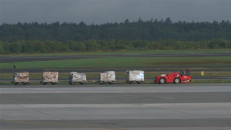 Ein-Gepäckwagen-Mit-Fünf-Vollgepackten-Waggons-Fährt-über-Den-Taxistreifen-Und-Verschwindet-Hinter-Einem-Flugzeug-In-Stockholm,-Arlanda