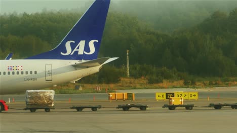Ein-Gepäcktransporter-Fährt-An-Einem-Flugzeug-Vorbei,-Das-Auf-Die-Landebahn-In-Stockholm,-Arlanda,-Zusteuert