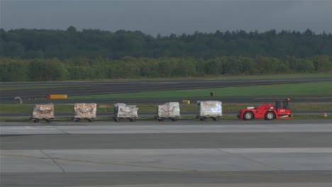 Airport-baggage-freight-trolley-moving-on-the-runway-across-a-passenger-aircraft-of-Stockholm-airport-in-Sweden