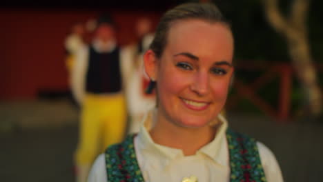 A-beautiful-Swedish-folk-dancer-performer-surrounded-by-fellow-dancers-smiles-at-the-camera-in-the-late-afternoon