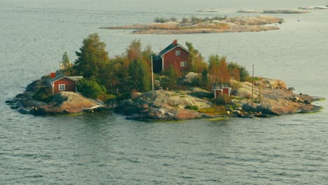 Wide-aerial-view-of-a-beautiful-dark-red-wooden-home-and-out-buildings-on-a-small-rocky-island