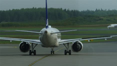 Nahaufnahme-Eines-Flugzeugs,-Das-Die-Tore-Zur-Landebahn-Verlässt,-Während-Im-Hintergrund-Ein-Kleines-Flugzeug-Abhebt