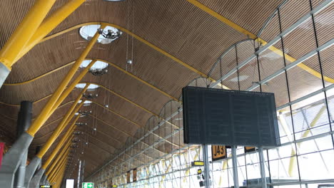 Flughafenterminal-Am-Internationalen-Flughafen-Madrid-Barajas,-Langsames-Hochkippen-Aus-Dem-Belebten-Gebäude,-Strömende-Menschen,-Die-Die-Einzigartige-Architektur-Des-Terminals-Mit-Holzverkleideter-Decke-Und-Großen-Fenstern-Offenbaren