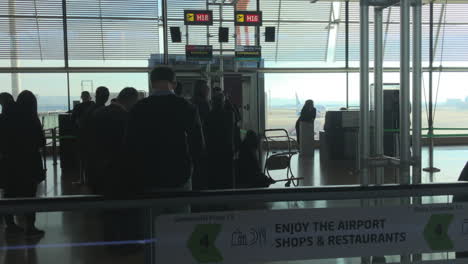 Sliding-dolly-shot-of-passengers-in-the-waiting-area-of-an-airport-to-board-their-airplanes,-boarding-gates-in-background