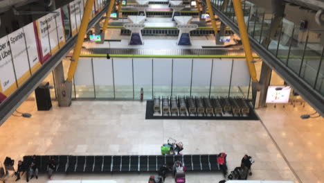 Aufschlussreiche-Aufnahme-Des-Flughafenterminalbereichs-Mit-Mehreren-Gepäckausgabebändern,-Langsame-Neigung-Nach-Oben,-Die-Das-Terminal-Mit-Passagieren-Und-Geschäften-Auf-Der-Oberen-Terminalebene-Am-Flughafen-Madrid-Barajas-Zeigt
