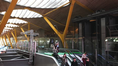 Modernes-Flughafenterminal-Mit-Menschen,-Die-Rolltreppen-Benutzen,-Zeitgenössisches-Architektonisches-Design,-Das-Stahl-Und-Holz-Mit-Großen-Durchscheinenden-Fenstern-In-Der-Decke-Kombiniert,-Reisen,-Transport-Und-Architektur