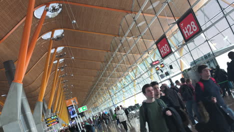 Flugbesatzungsmitglieder,-Die-Vorbeifliegen,-Gekippter-Dolly-Im-Terminalbereich-Des-Flughafens,-Mit-Passagieren-Im-Hintergrund,-Menschen,-Die-Zu-Den-Flugsteigen-Am-Flughafen-Madrid-Barajas-Gehen